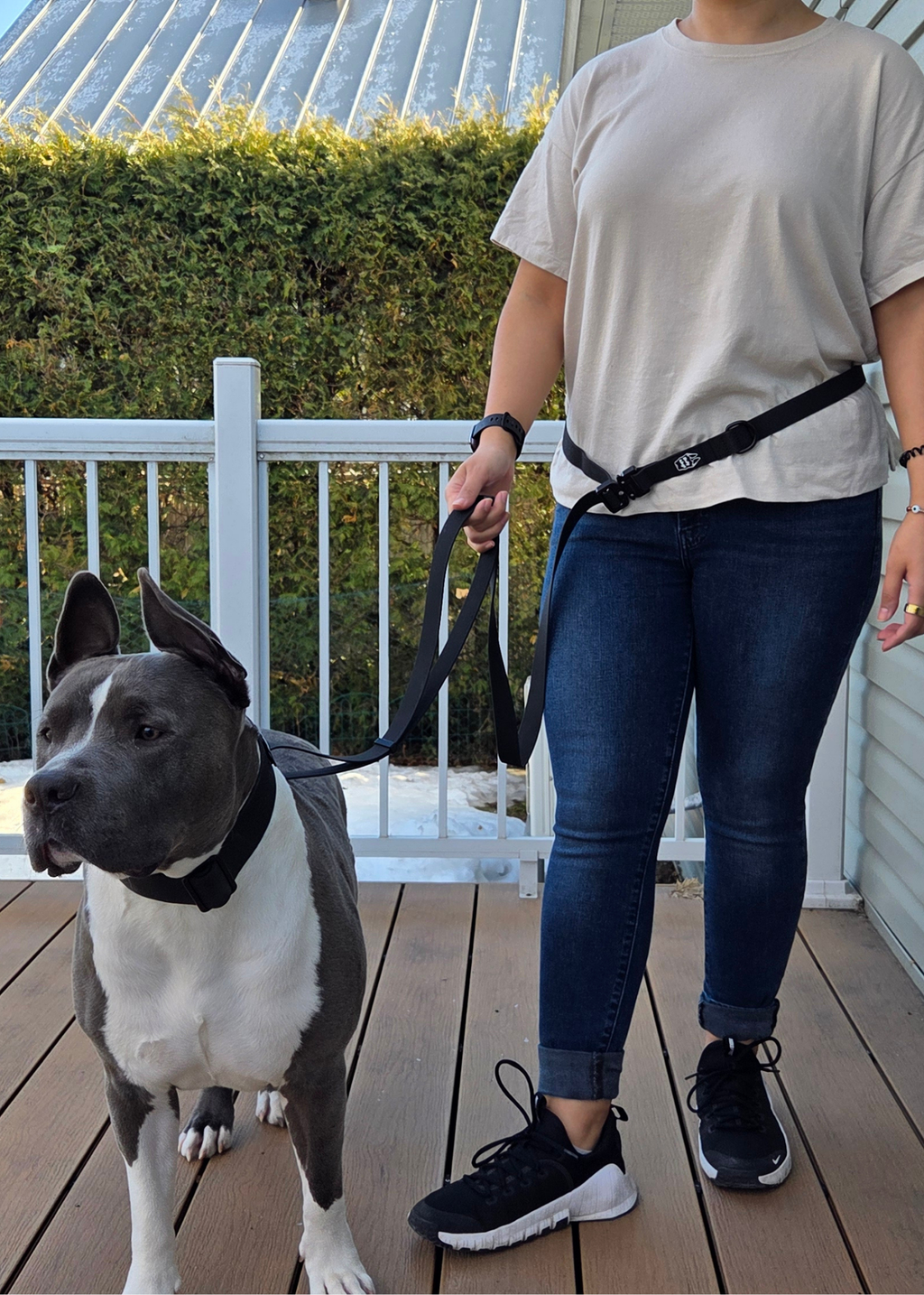 Person walking a dog on a leash with a white shirt and dark pants, standing on a wooden deck.