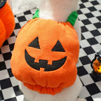 White dog wearing an orange pumpkin costume with black face on a checkered floor.