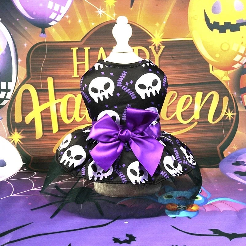 Halloween-themed dog dress with skull pattern and purple bow on a decorative background.