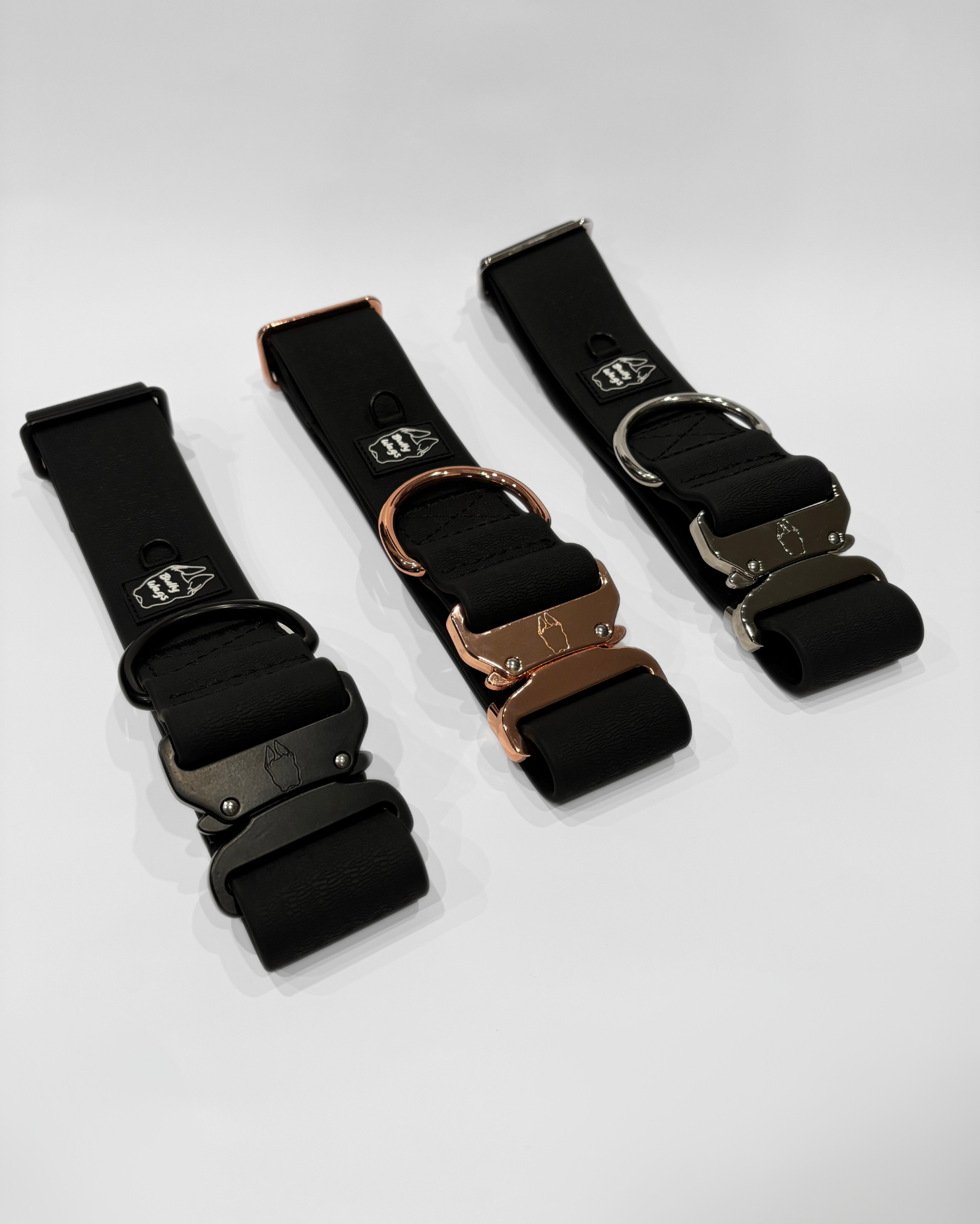 Three black dog collars with different metal buckles on a white background