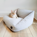 Cat lying on a gray pet bed with a visible brand logo on a wooden floor.