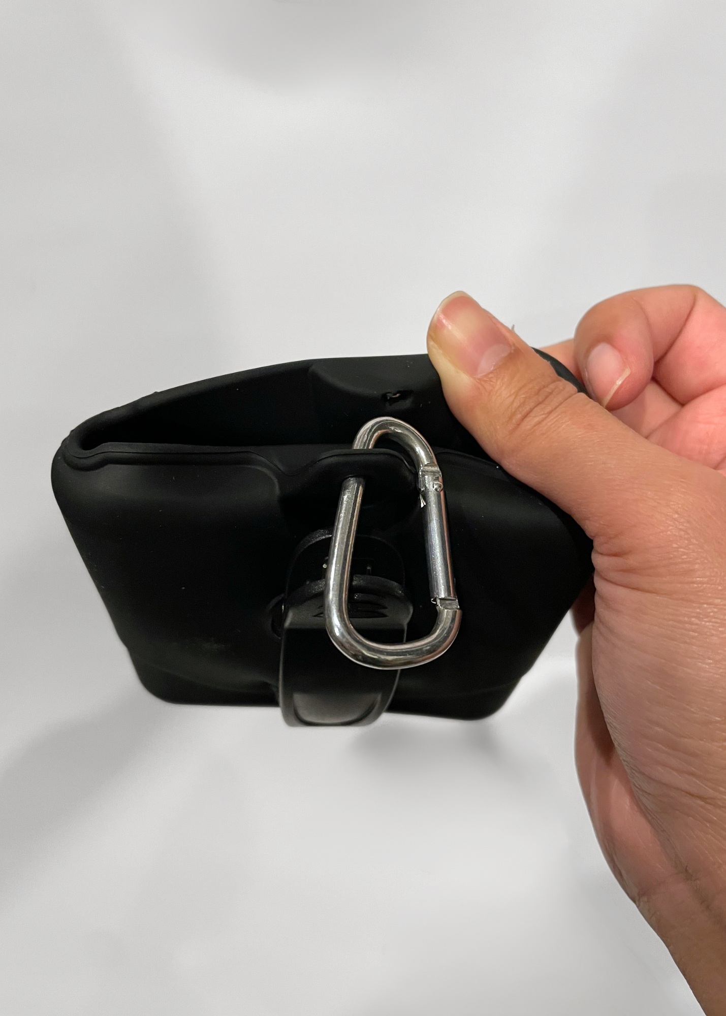 Hand holding a black treat bag with a carabiner attachment on a white background