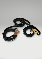 Three black dog leash with gold buckles on a gray background
