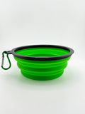 Green collapsible silicone dog bowl with black rim and carabiner on a white background