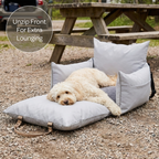 Dog lying on a gray pet bed with pillows outdoors near a wooden picnic table.