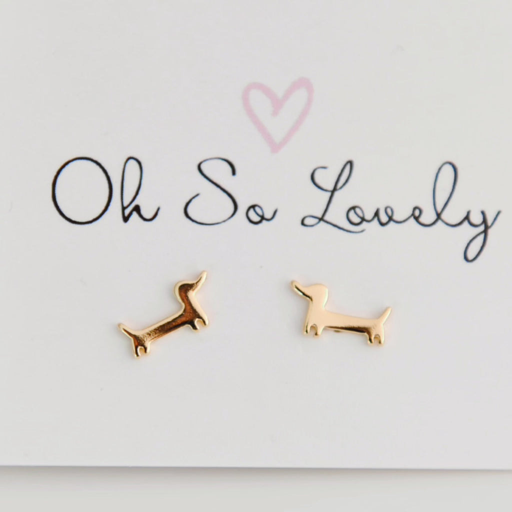 Gold dog-shaped earrings on a 'Oh So Lovely' card.