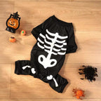 Black baby romper with skeleton design on a wooden floor with Halloween decorations.