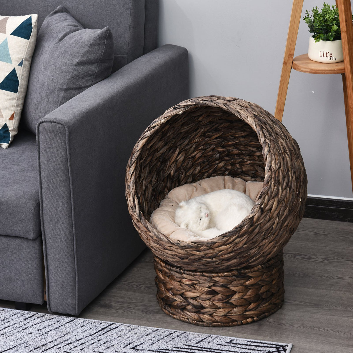 Woven pet bed in a living room setting with a gray sofa and decorative elements.