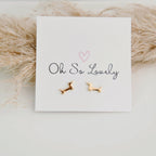 Gold dog-shaped earrings on a 'Oh So Lovely' card with a soft beige background