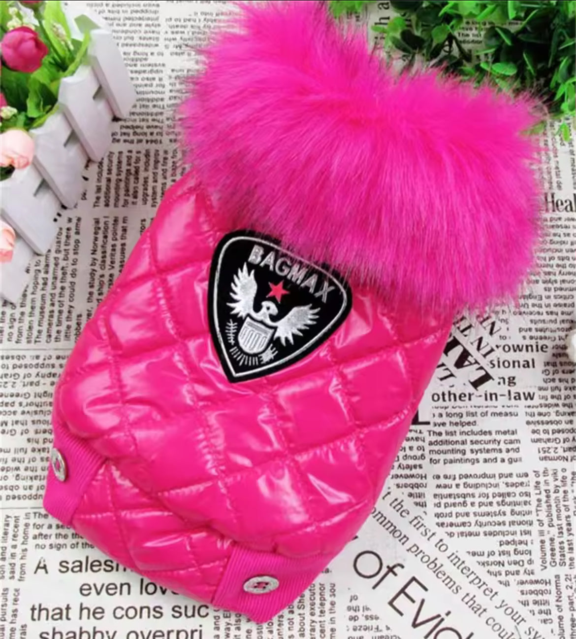 Pink dog coat with a large fur pom-pom on a newspaper background