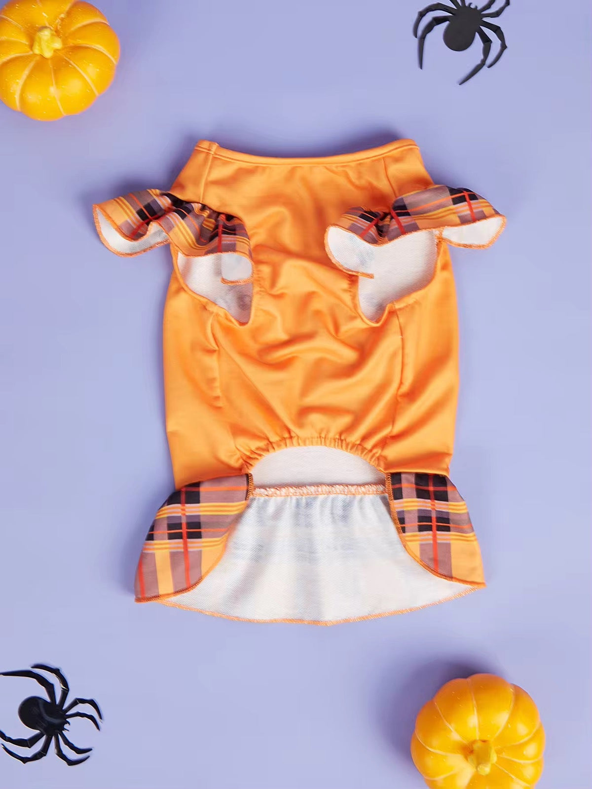 Dog Halloween costume with orange top and plaid trim on a purple background with pumpkins and spiders.
