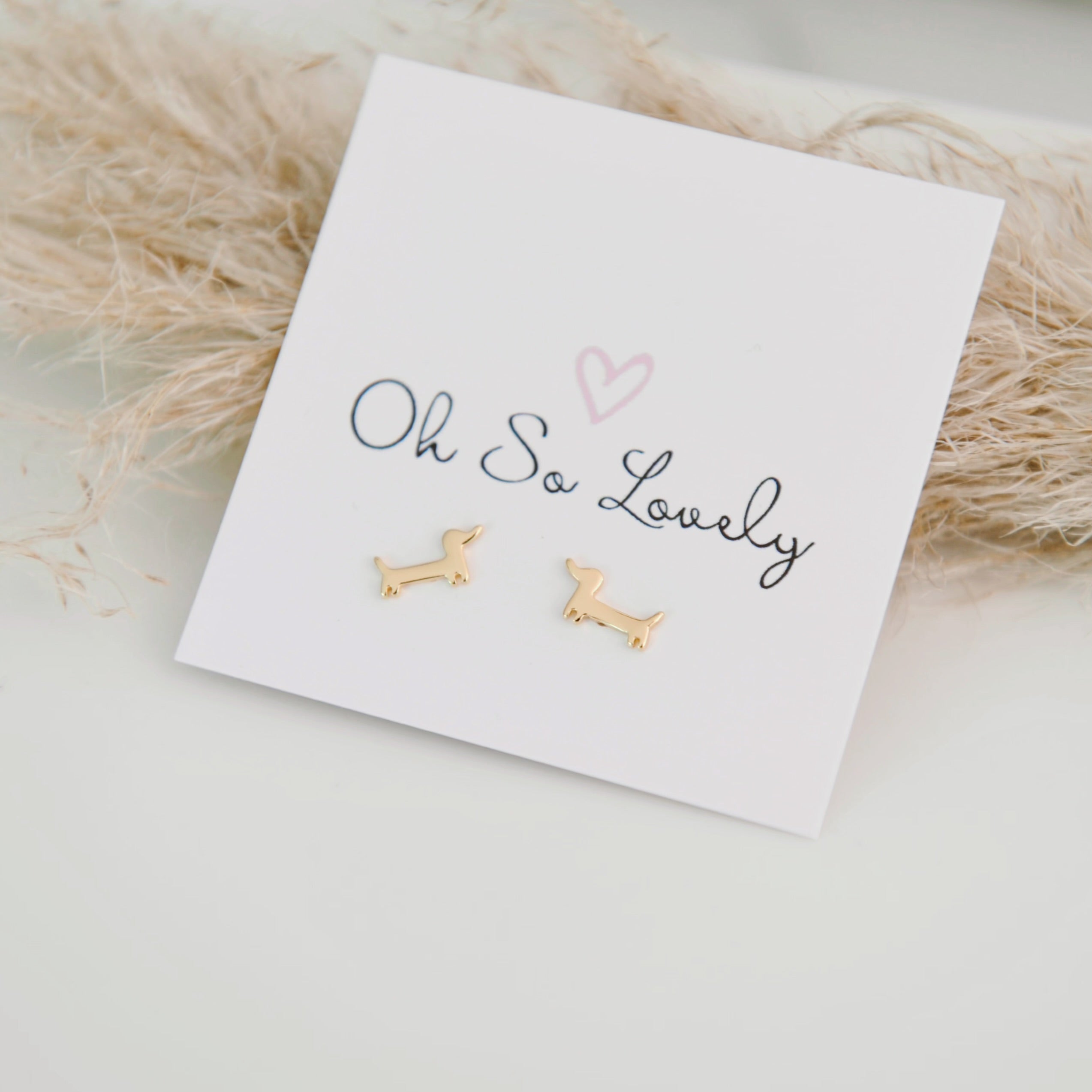 Gold dog-shaped earrings on a 'Oh So Lovely' card with a soft background