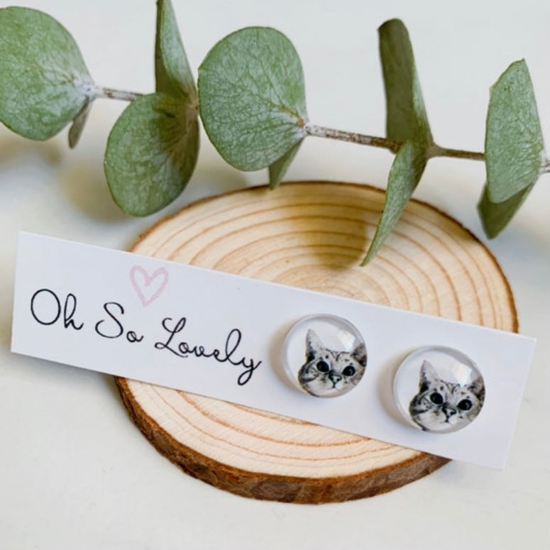 Cat-themed earrings on a wooden block with eucalyptus leaves