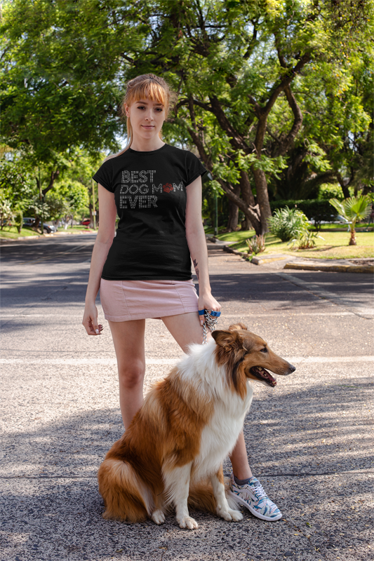 Woman wearing a black t-shirt with 'Best Dog Mom Ever' text, standing with a dog on a street.