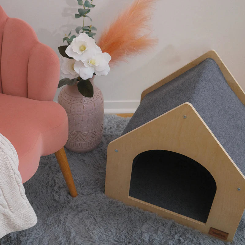 Pet house on a gray carpet with a pink chair and decorative elements in the background