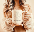 Person holding a white mug with 'DOG MOM' and a paw print design.