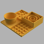 A yellow slow feeder set on a light gray background, featuring a bowl, a tray with small raised spheres, a spiral insert, and a hexagonal grid mat.