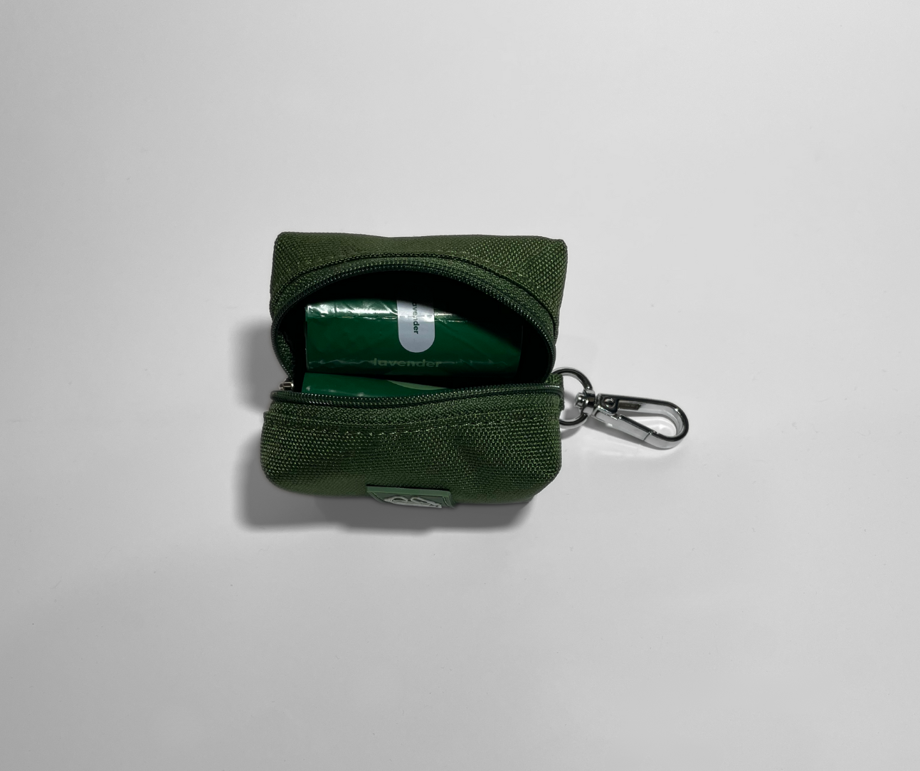 Green keychain pouch with a poop bag rolls inside on a light gray background