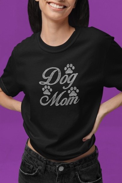 Person wearing a black 'Dog Mom' t-shirt with rhinestone accents on a purple background