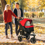 Couple walking a small dog in a red stroller through a park with autumn leaves.