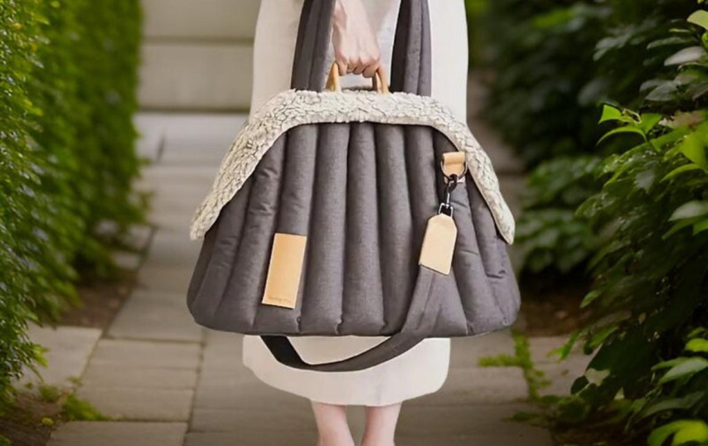Person holding a gray quilted pet carrier with decorative trim in an outdoor setting