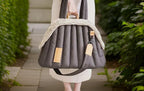 Person holding a gray quilted pet carrier with decorative trim in an outdoor setting