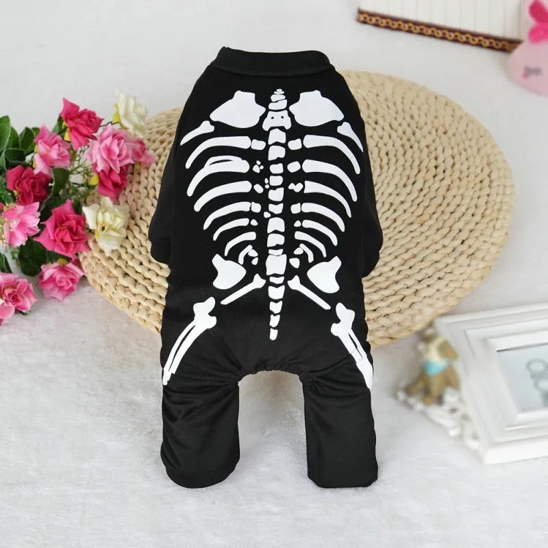 Black pet onesie with white skeleton design on a white surface with flowers and a woven basket in the background.