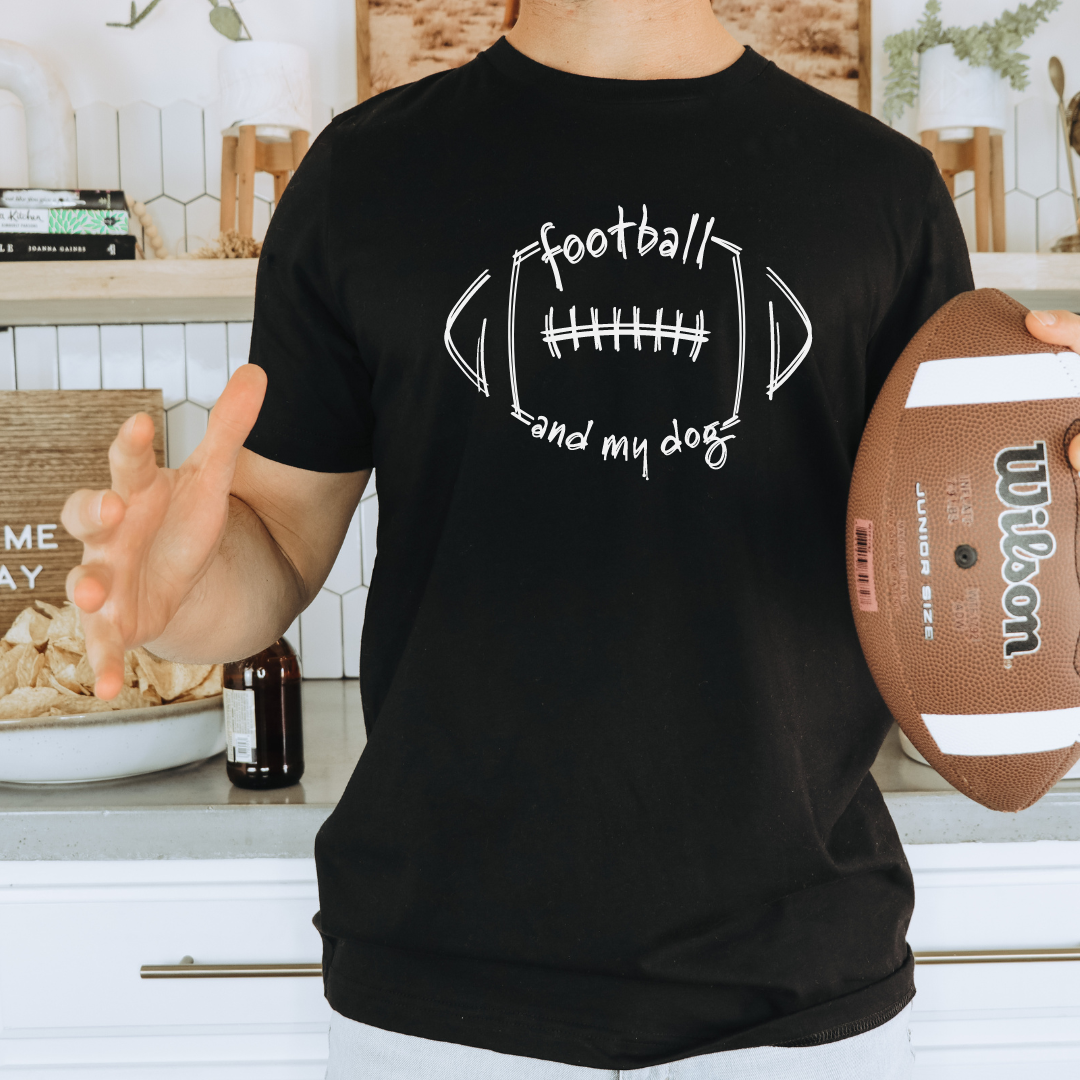 Person wearing a black t-shirt with 'football and my dog' design, holding a Wilson football in a kitchen.