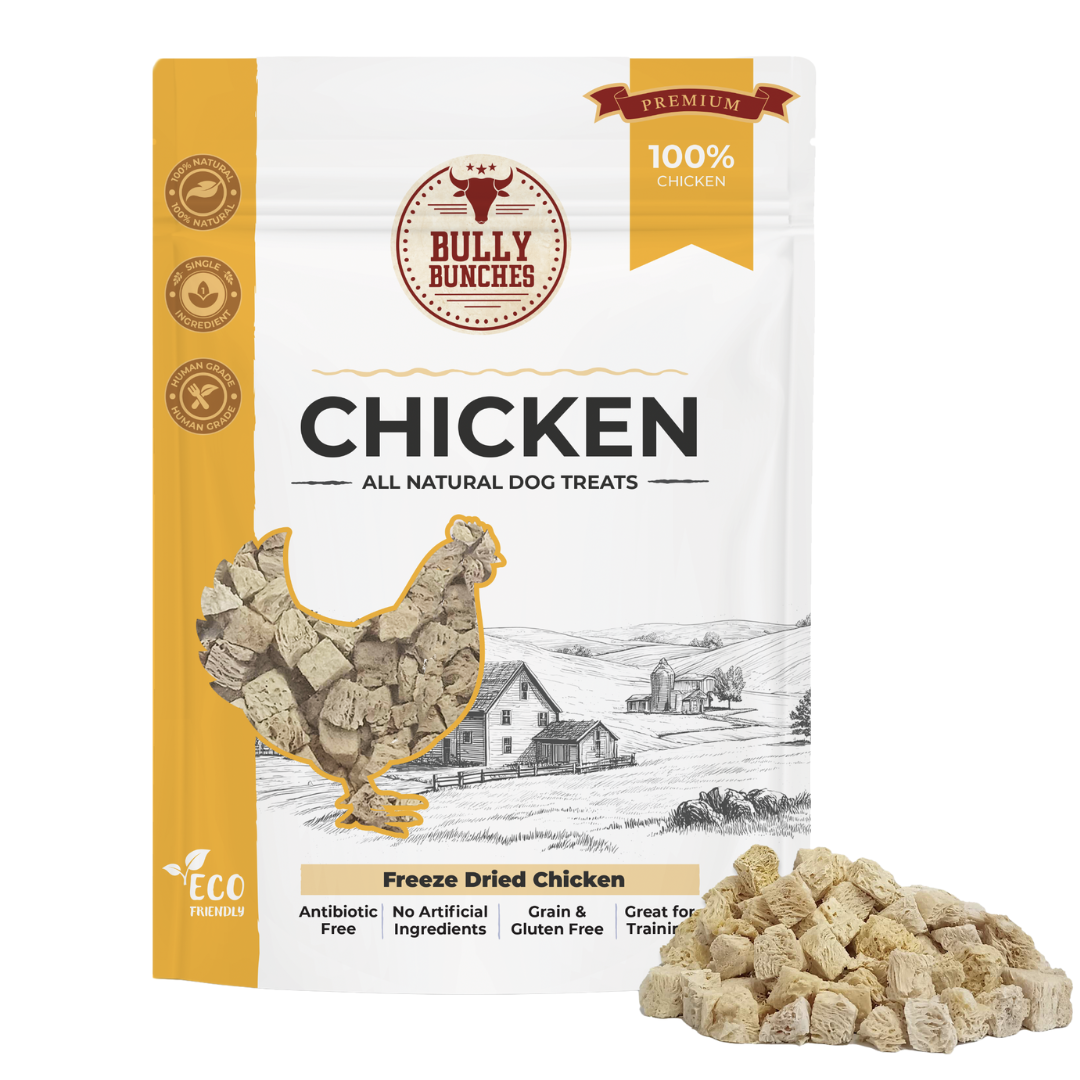 A stand-up pouch of Bully Bunches Freeze Dried Chicken dog treats, shown on a white background with a small pile of the beige freeze-dried treats in front. The package is white and mustard yellow with a chicken-shaped cutout showing the treats inside and a black-and-white farm illustration.
