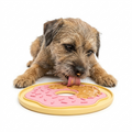 Dog playing with a pink and yellow donut-shaped lick mat on a white background