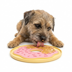 Dog playing with a pink and yellow donut-shaped lick mat on a white background