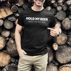 Person wearing a black t-shirt with text  Hold my beer while I pet this dog standing in front of stacked logs.