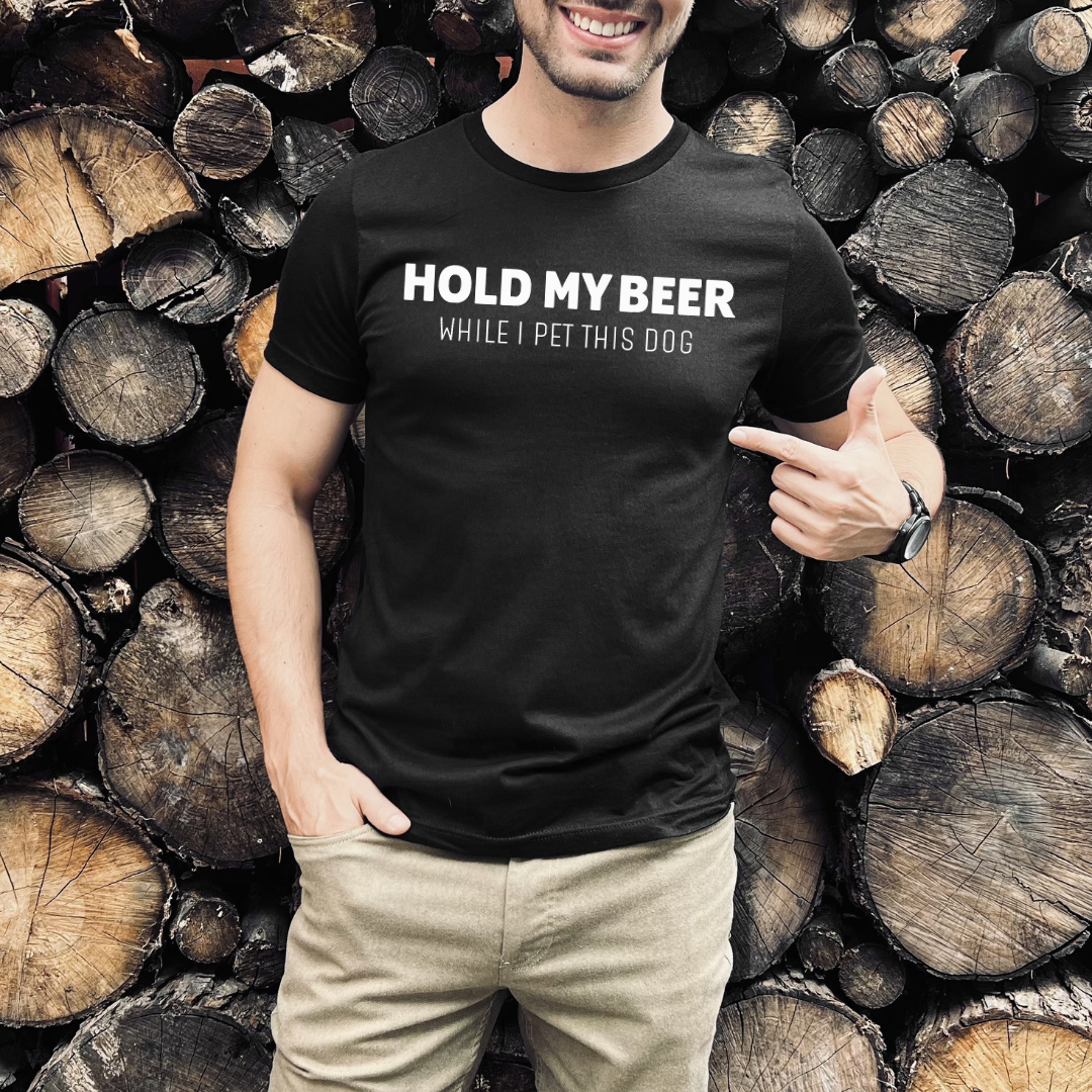 Person wearing a black t-shirt with text  Hold my beer while I pet this dog standing in front of stacked logs.