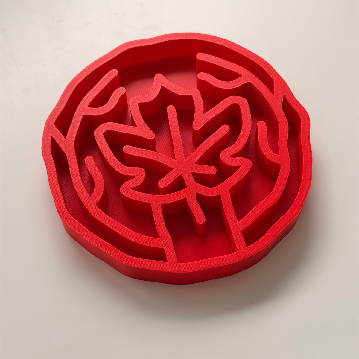 A bright red slow feeding bowl with maple leaf design, shown on a clean white background.