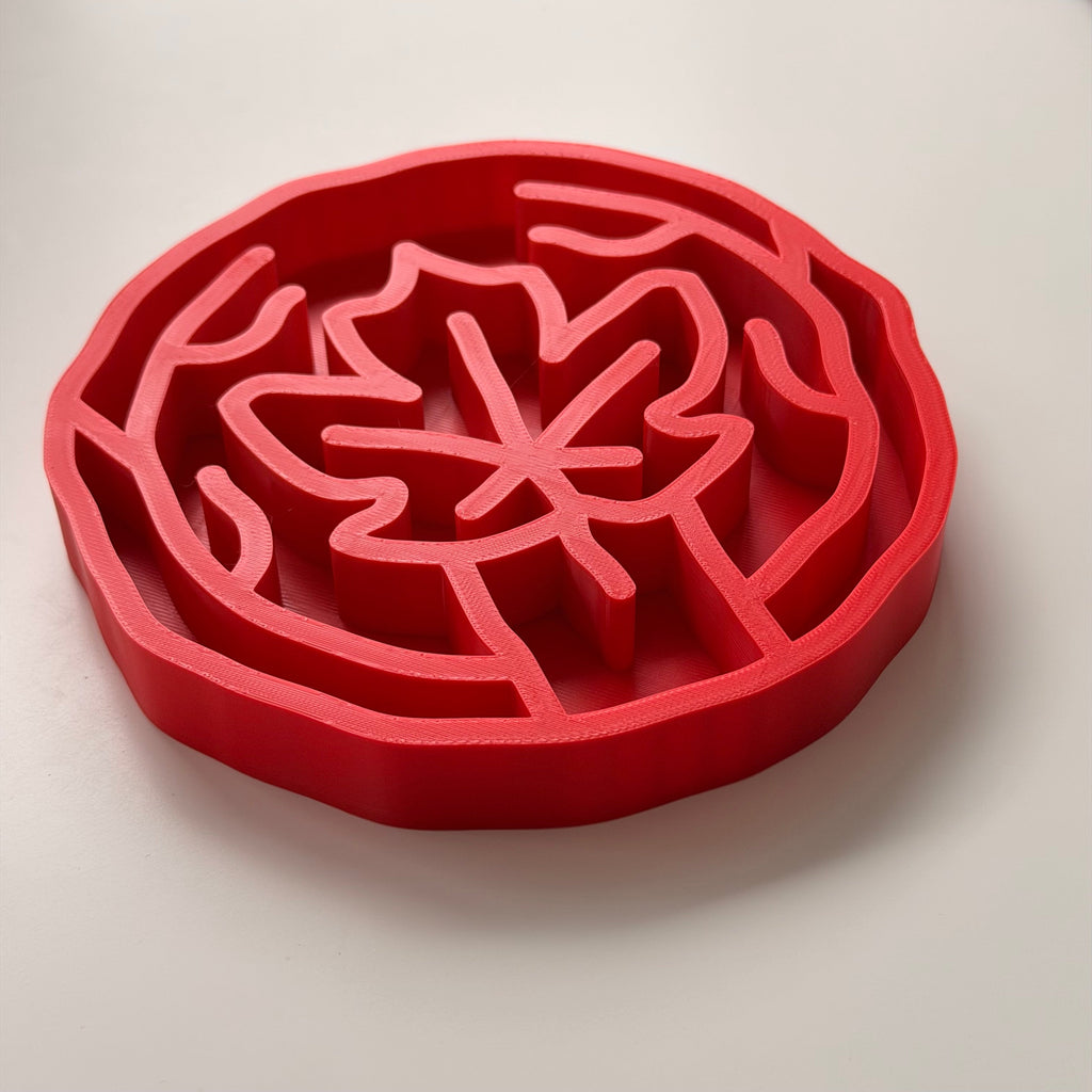 A red slow feeding bowl with maple leaf design, shown on a clean white background.