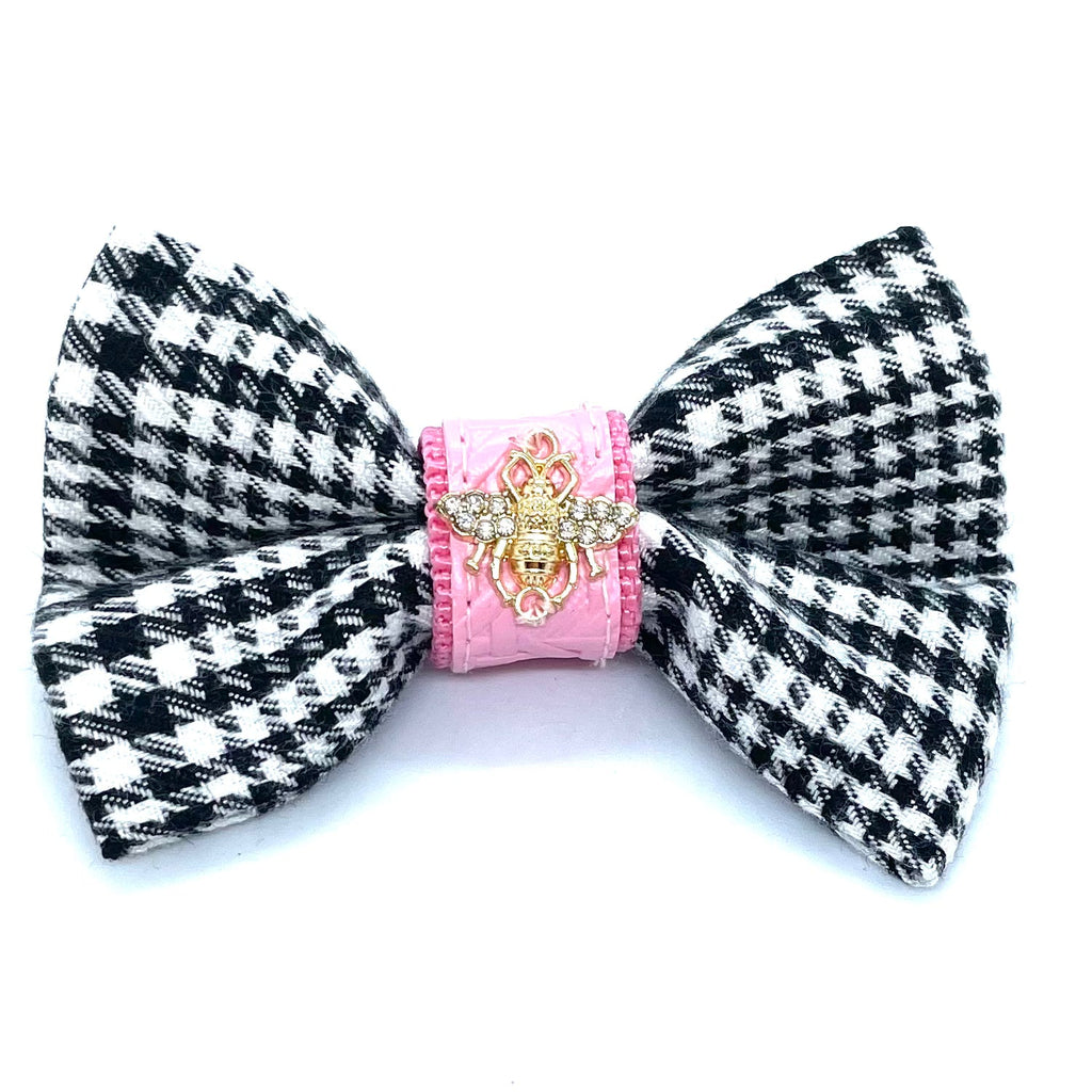 Black and white houndstooth patterned bow with pink center and gold emblem on a white background