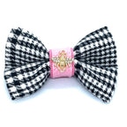 Black and white houndstooth patterned bow with pink center and gold emblem on a white background