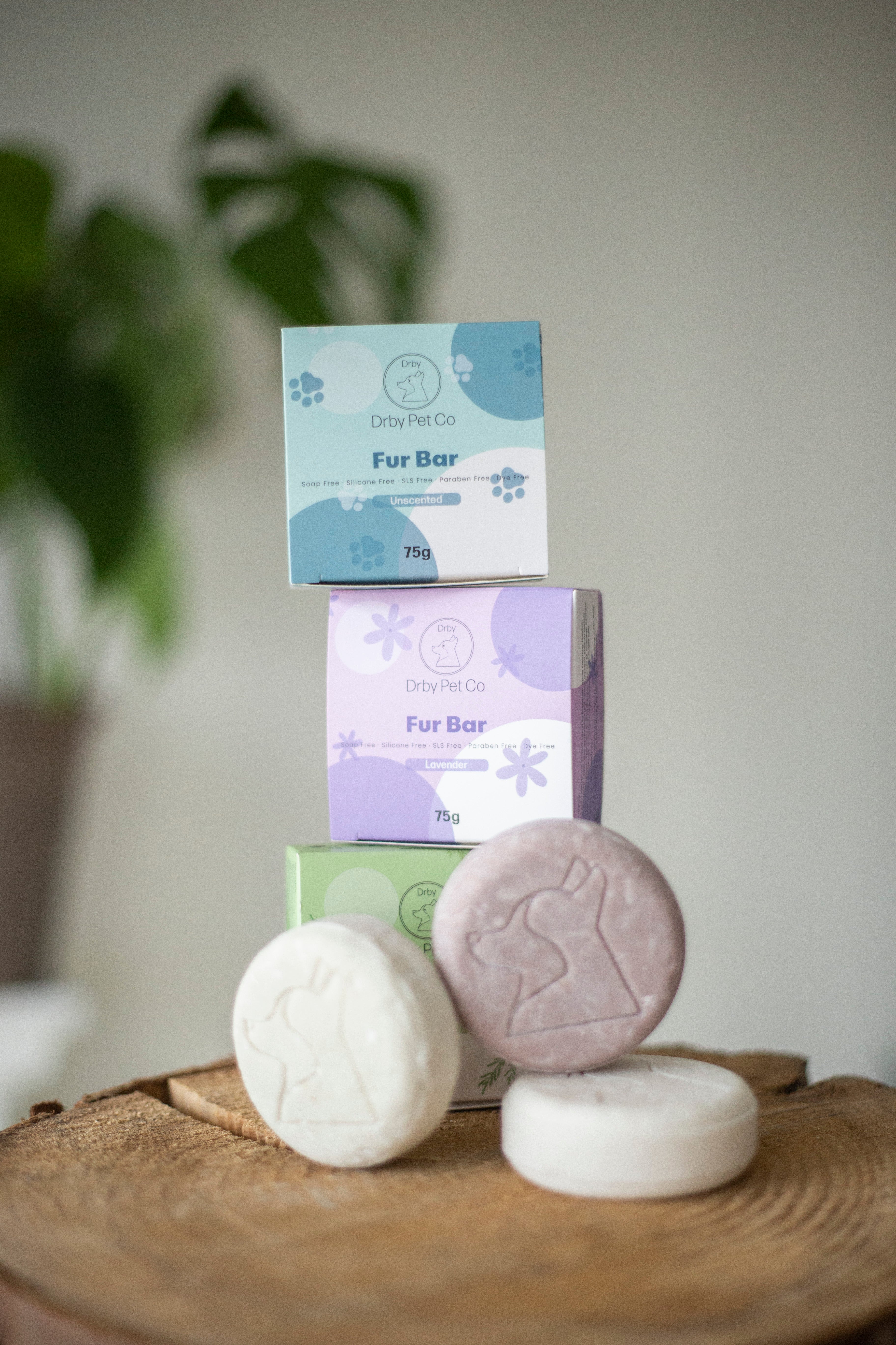 Pet care products including bath bars and boxes on a wooden surface with a blurred plant background.