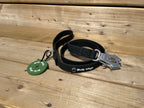 Black dog leash with metal clip and green tag on wooden surface