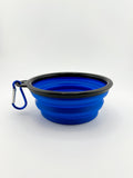 Blue silicone travel bowl with black rim and carabiner on a white background