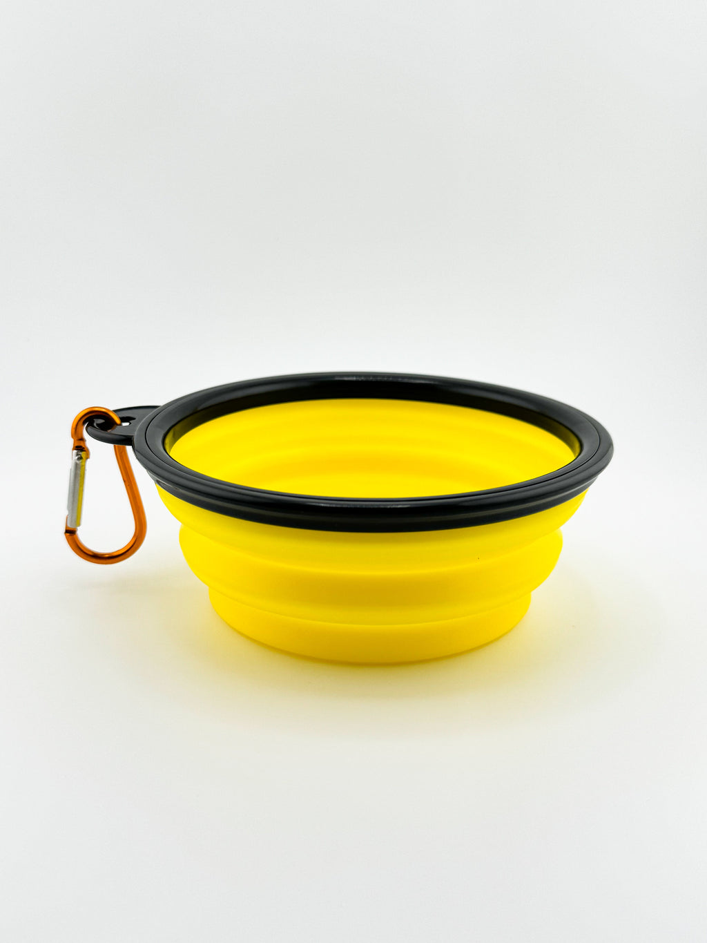 Yellow silicone dog bowl with black rim and carabiner on a white background