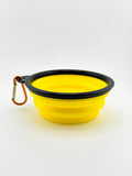 Yellow silicone dog bowl with black rim and carabiner on a white background