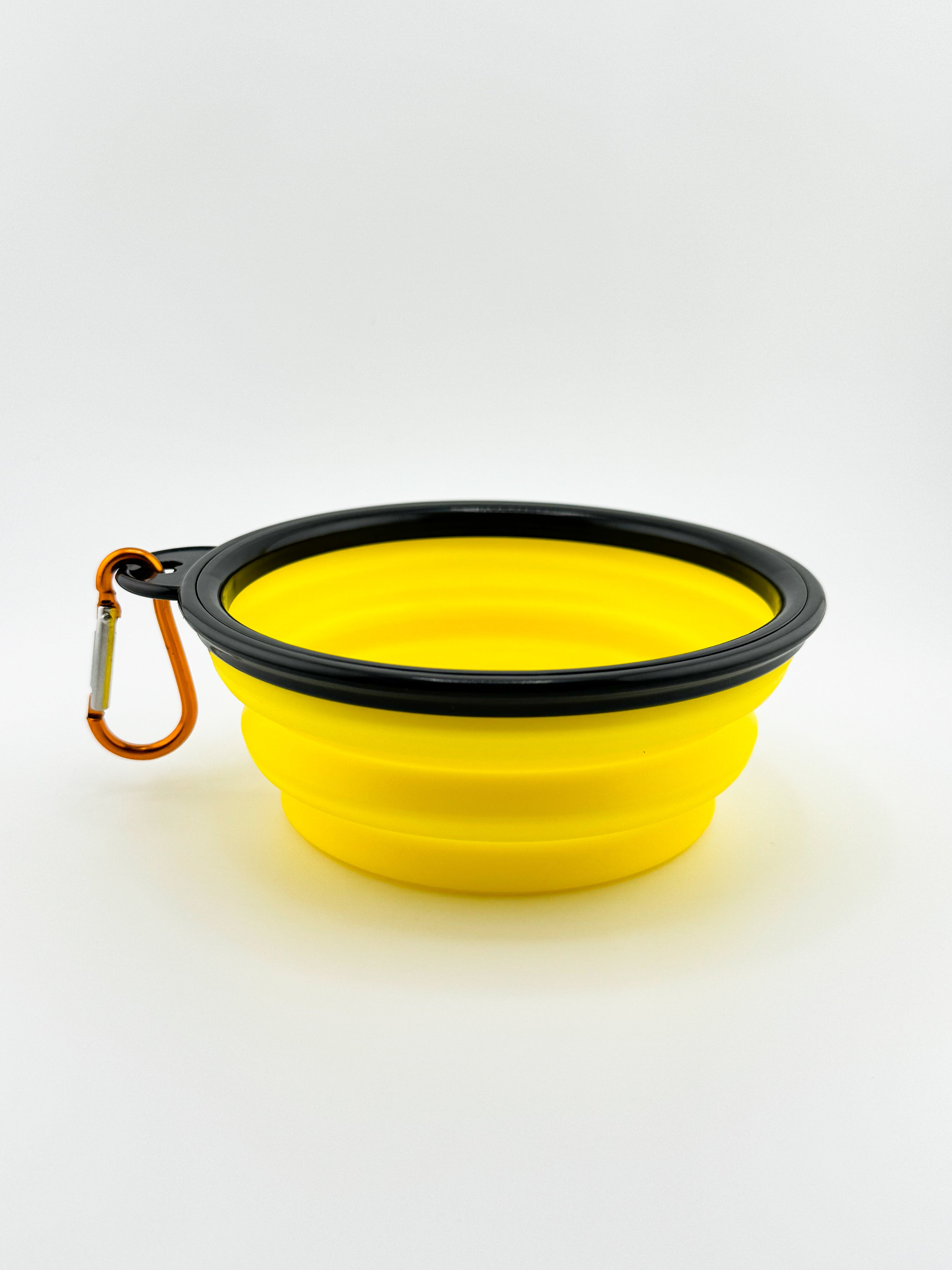 Yellow silicone dog bowl with black rim and carabiner on a white background