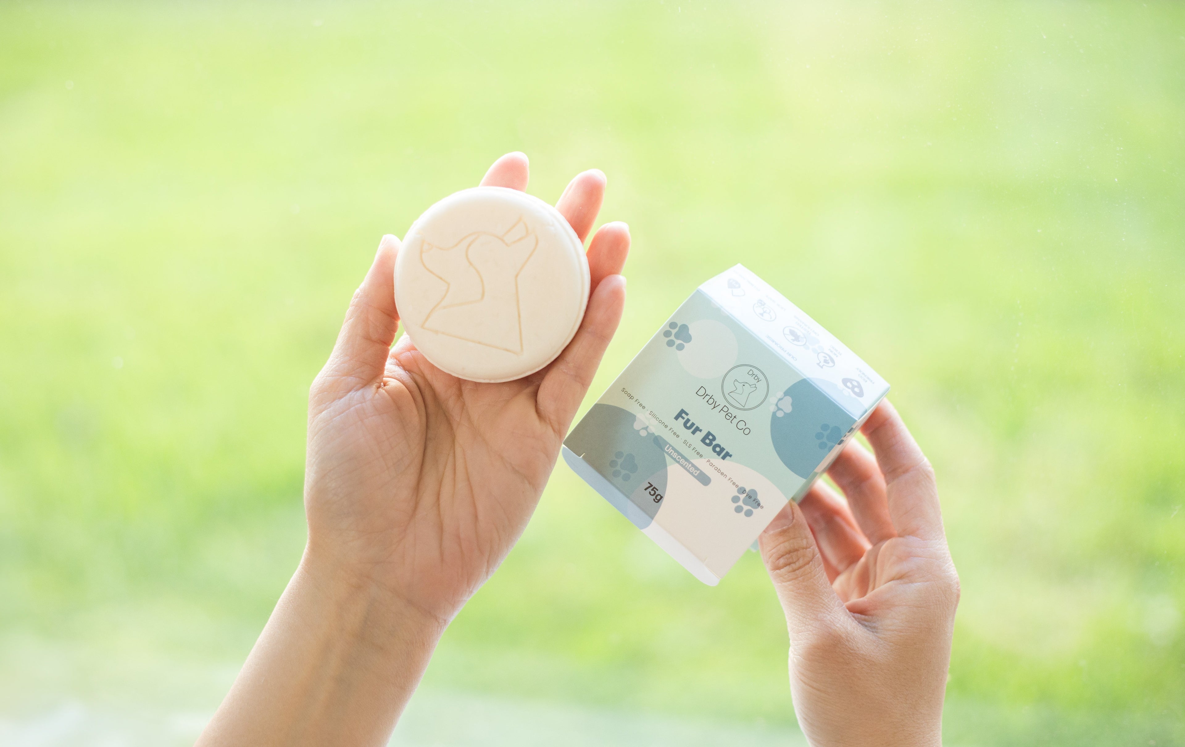Person holding a soap and its packaging against a blurred green outdoor background