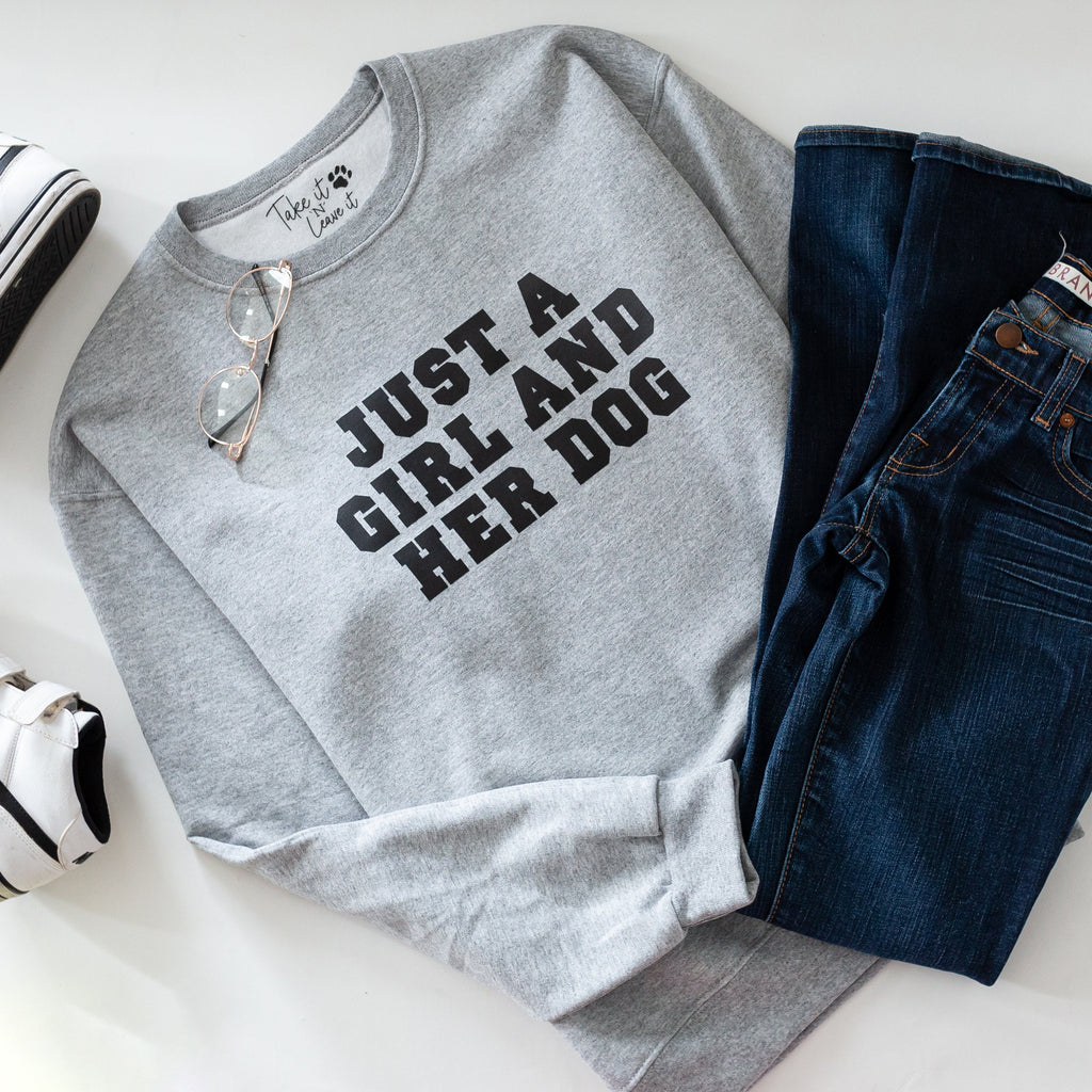 Gray sweatshirt with 'Just a Girl and Her Dog' text, paired with jeans and sneakers on a white surface.