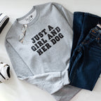 Gray sweatshirt with 'Just a Girl and Her Dog' text, paired with jeans and sneakers on a white surface.