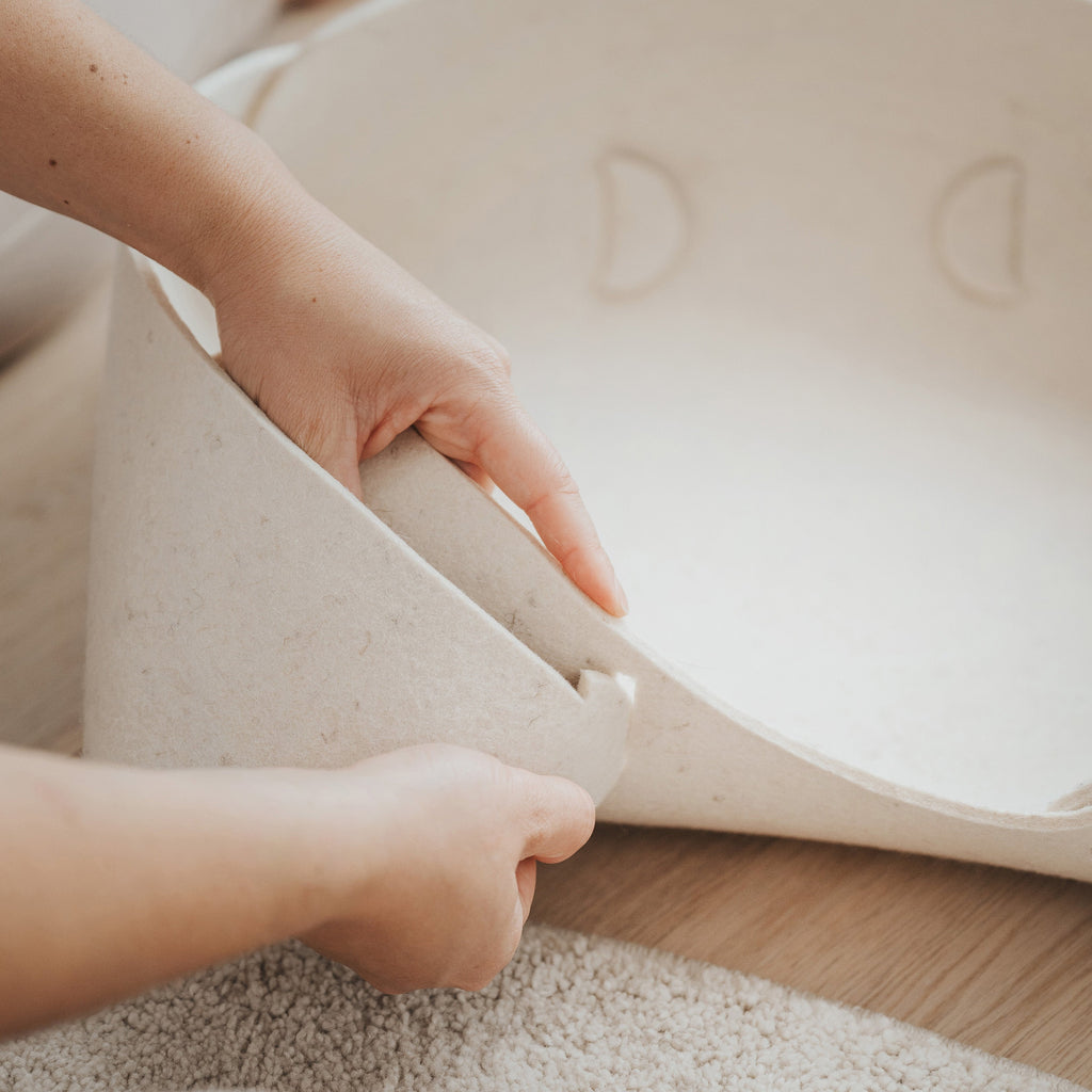 Person adjusting a pet bed on a wooden floor