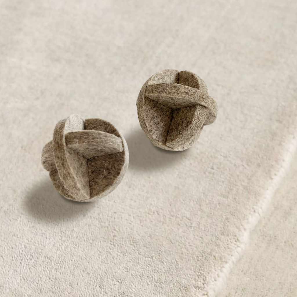 Two brown felted cat ball on a beige fabric background
