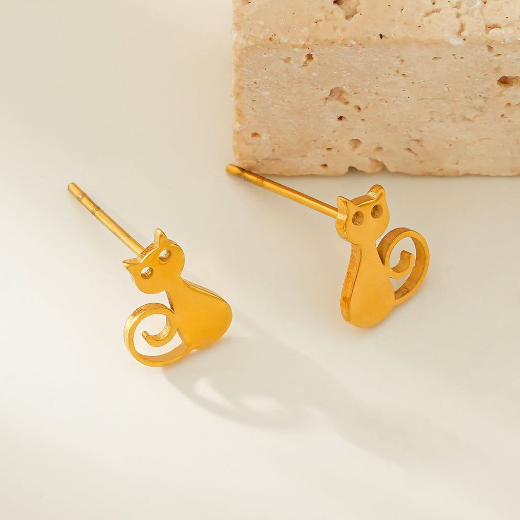 Gold cat-shaped earrings on a beige background