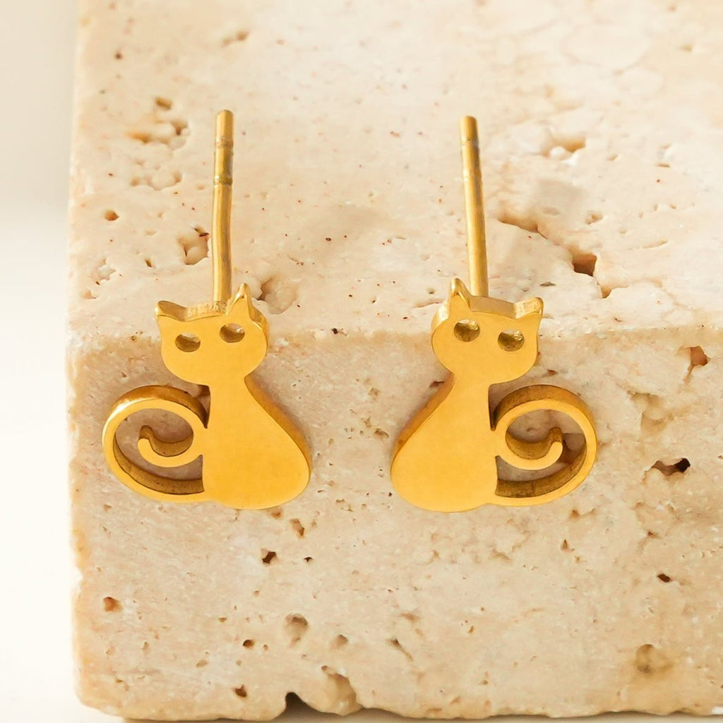 Gold cat-shaped earrings on a textured beige surface